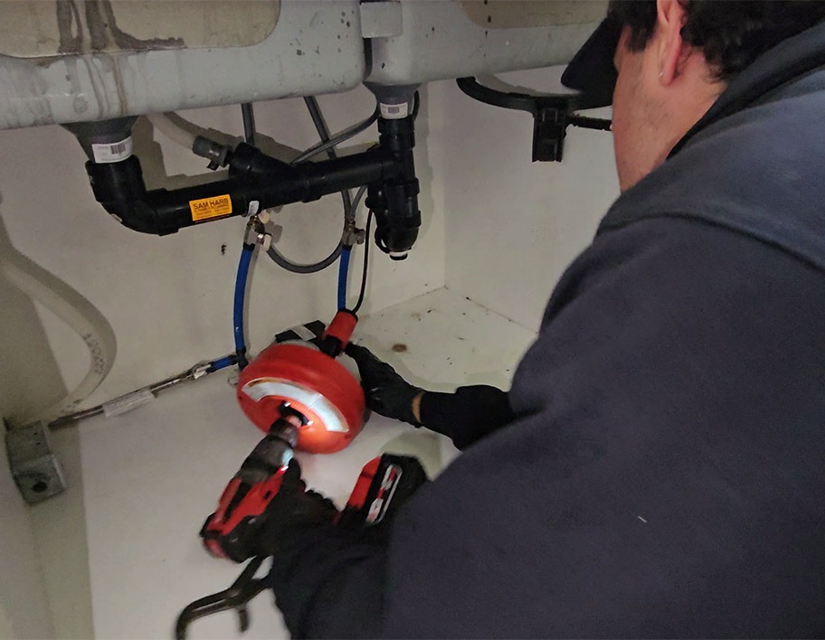 Plumber using drain cleaning equipment on a kitchen sink in Hamilton