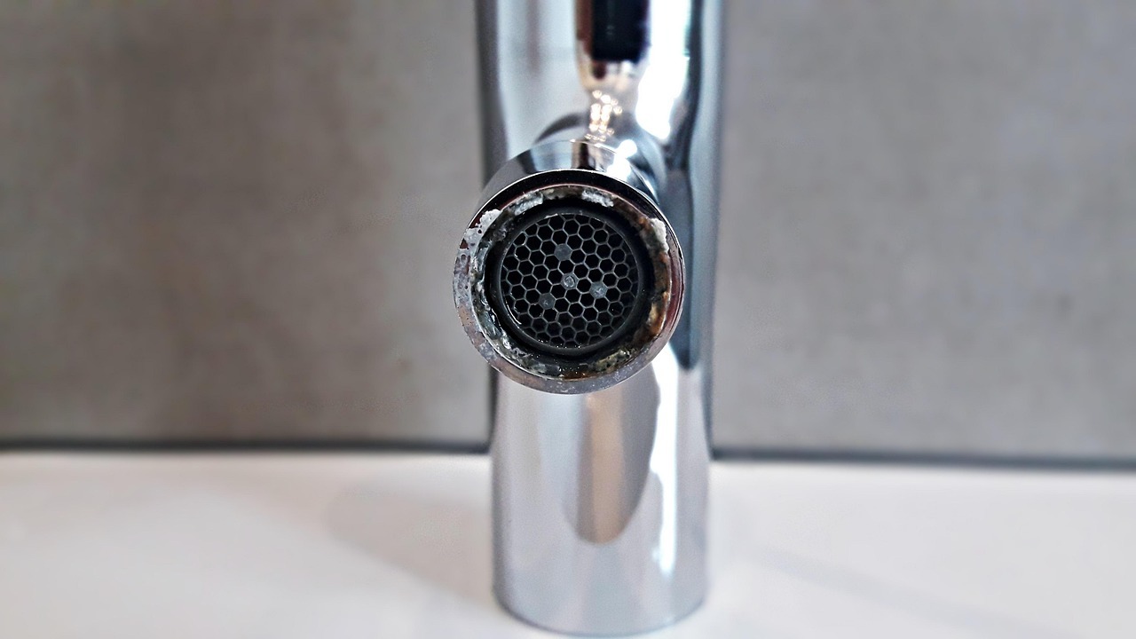 White mineral deposits and calcification around a chrome faucet aerator.