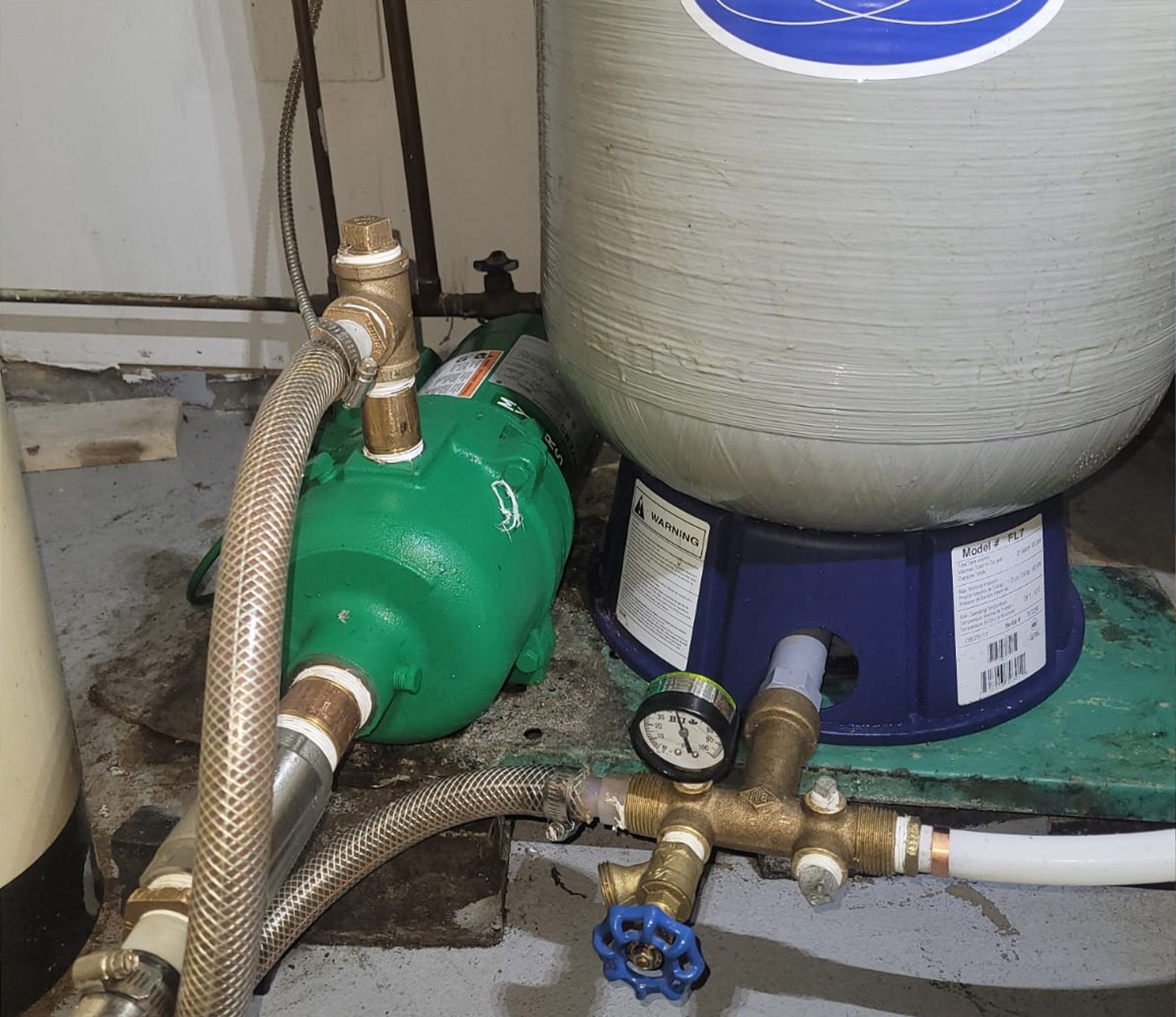 Green residential well jet pump installed beside a grey pressure tank with gauge and plumbing connections