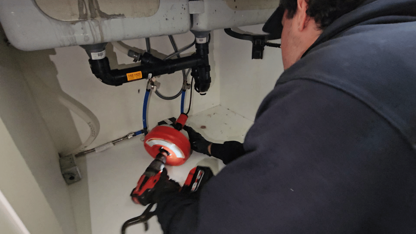 Plumber using drain cleaning equipment under a kitchen sink